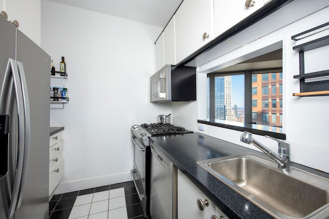 kitchen with appliances with stainless steel finishes, dark countertops, a sink, dark tile patterned flooring, and white cabinetry