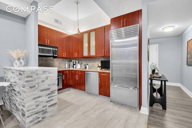 kitchen featuring stainless steel appliances, decorative backsplash, glass insert cabinets, a sink, and baseboards