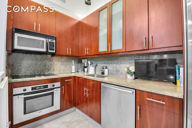 kitchen featuring appliances with stainless steel finishes, a sink, tasteful backsplash, and glass insert cabinets