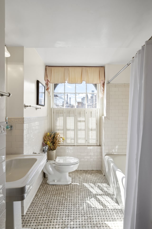 333 E 68th Street Penthouse, New York City, NY 10065 - bathroom featuring toilet, tile walls, shower / bath combo with shower curtain, and wainscoting