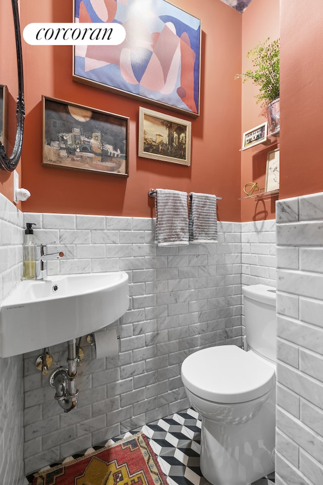 bathroom with wainscoting, toilet, a sink, and tile walls