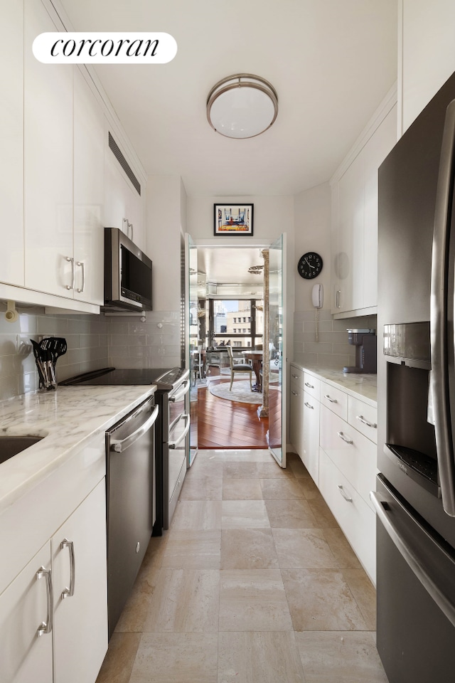 kitchen featuring white cabinets, backsplash, light stone countertops, and appliances with stainless steel finishes
