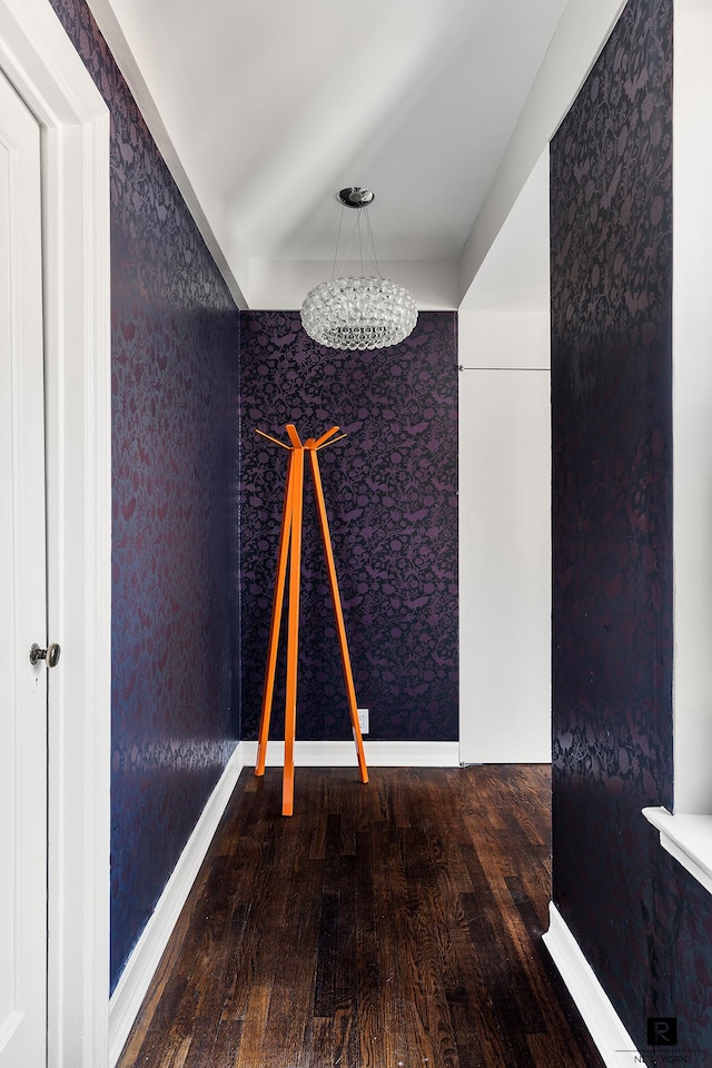 unfurnished room with baseboards, wood finished floors, wallpapered walls, and an inviting chandelier