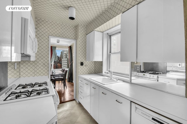kitchen with decorative backsplash, a sink, light countertops, white cabinets, and white appliances