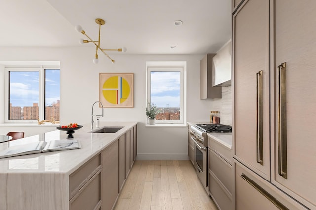 kitchen with high end stainless steel range, a sink, light wood-style floors, a peninsula, and gray cabinetry