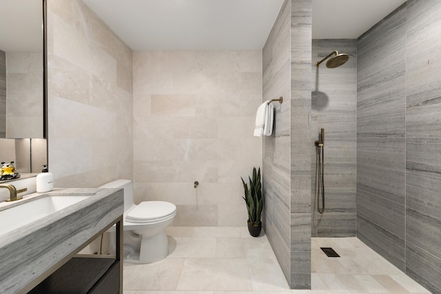 full bath with tile patterned floors, a tile shower, tile walls, toilet, and vanity