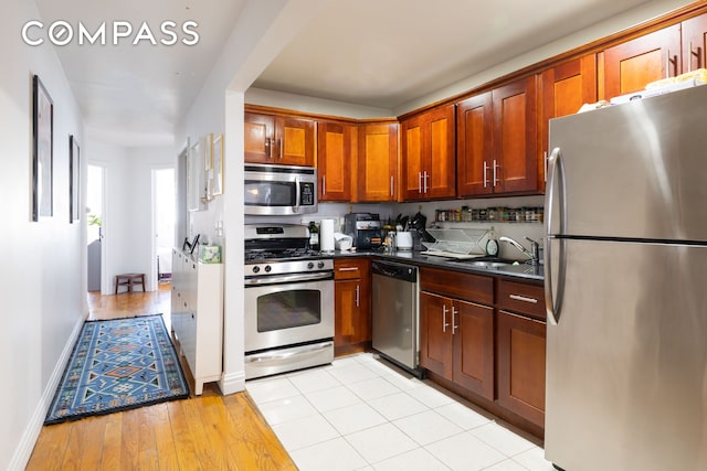 kitchen featuring dark countertops, a sink, light wood-style floors, baseboards, and appliances with stainless steel finishes