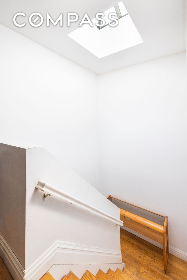 stairs with wood finished floors, a skylight, and baseboards