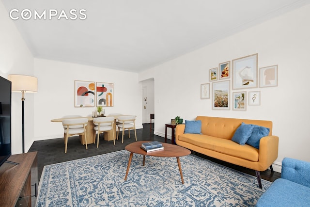 living area with baseboards, ornamental molding, and arched walkways