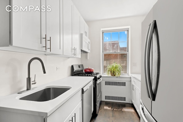kitchen with radiator, dark wood-style floors, light countertops, a sink, and appliances with stainless steel finishes