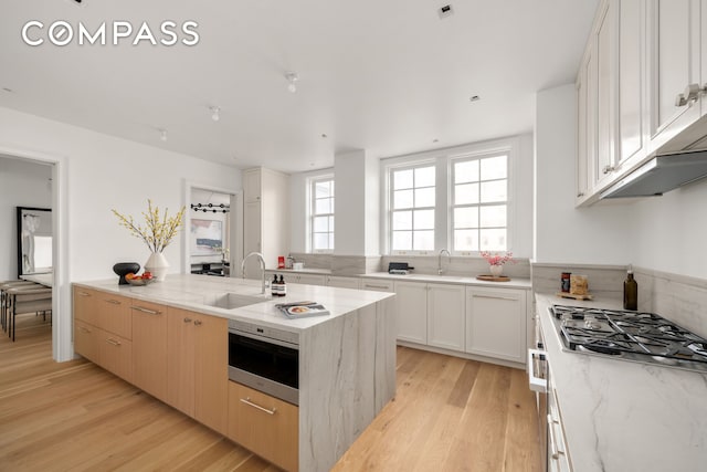 kitchen with a sink, light wood-style flooring, stainless steel gas cooktop, and light stone counters