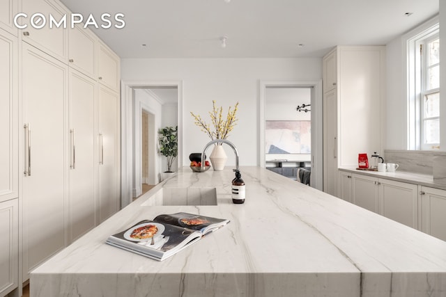 kitchen featuring light stone counters, white cabinetry, and a sink