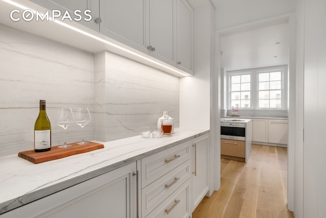 kitchen with light wood-type flooring, light stone counters, white cabinets, and a sink