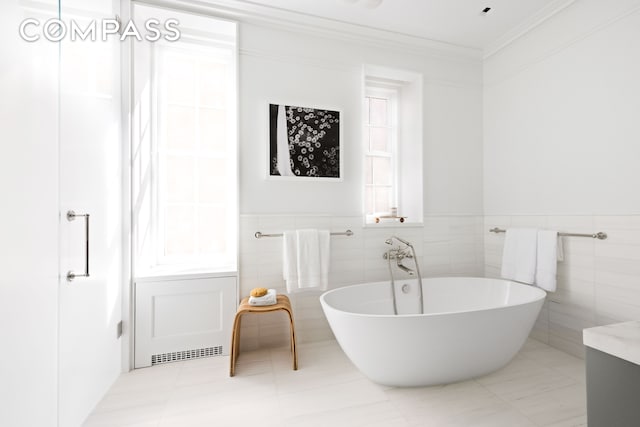 bathroom with a freestanding tub, tile walls, ornamental molding, and a wainscoted wall
