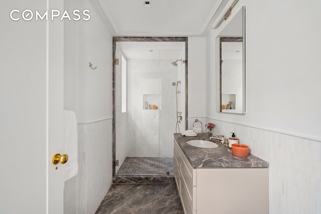 bathroom with marble tiled floors, a stall shower, wainscoting, vanity, and ornamental molding