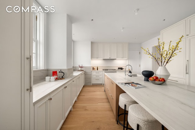 kitchen with light wood-type flooring, light stone counters, white cabinets, and a kitchen bar