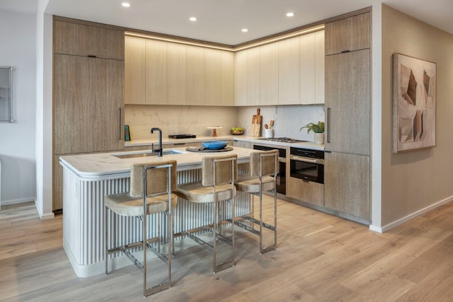 kitchen featuring stainless steel appliances, a center island with sink, a sink, modern cabinets, and tasteful backsplash