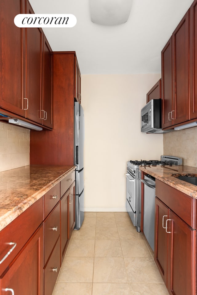 kitchen featuring stainless steel appliances, tasteful backsplash, light stone counters, and reddish brown cabinets