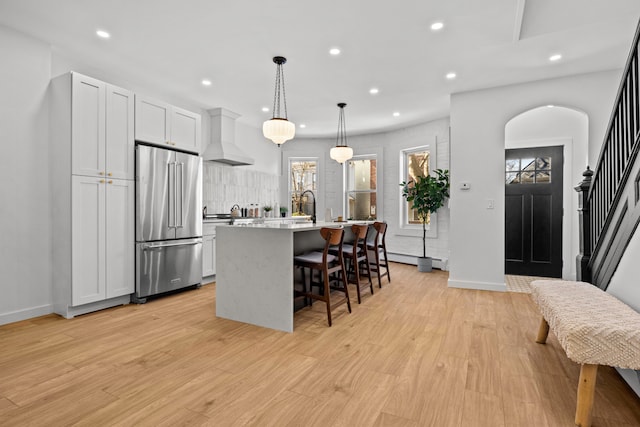 kitchen with custom exhaust hood, high end refrigerator, recessed lighting, tasteful backsplash, and a center island with sink