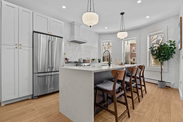 kitchen featuring tasteful backsplash, high end refrigerator, premium range hood, light wood finished floors, and recessed lighting