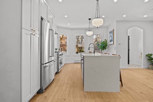 kitchen with recessed lighting, light wood-type flooring, a center island with sink, and high quality appliances