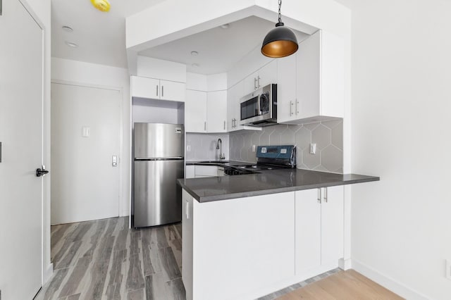 kitchen featuring stainless steel appliances, light wood finished floors, a peninsula, dark countertops, and backsplash