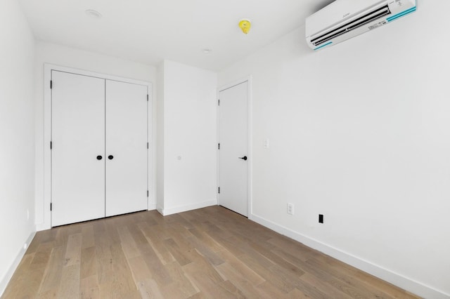 unfurnished bedroom featuring a wall unit AC, light wood finished floors, and baseboards
