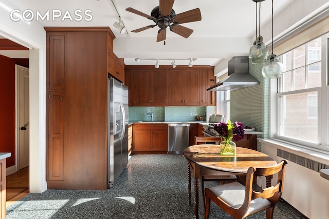 kitchen featuring rail lighting, wall chimney exhaust hood, appliances with stainless steel finishes, and radiator