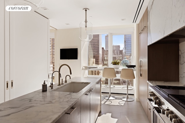 kitchen featuring a sink, range with two ovens, hanging light fixtures, light stone countertops, and light tile patterned floors