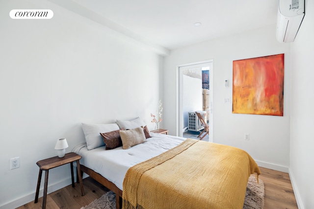bedroom with a wall unit AC, wood finished floors, and baseboards
