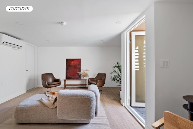 sitting room featuring an AC wall unit, light wood-style flooring, and baseboards