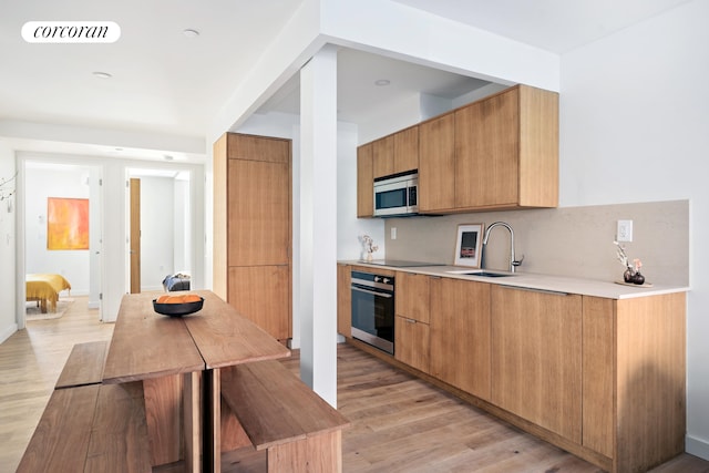 kitchen with appliances with stainless steel finishes, modern cabinets, backsplash, light wood-style flooring, and a sink