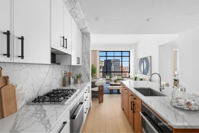 kitchen with light stone counters, backsplash, a sink, stainless steel appliances, and light wood-style floors