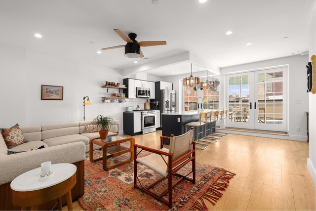 living room featuring recessed lighting, ceiling fan with notable chandelier, and light wood-type flooring