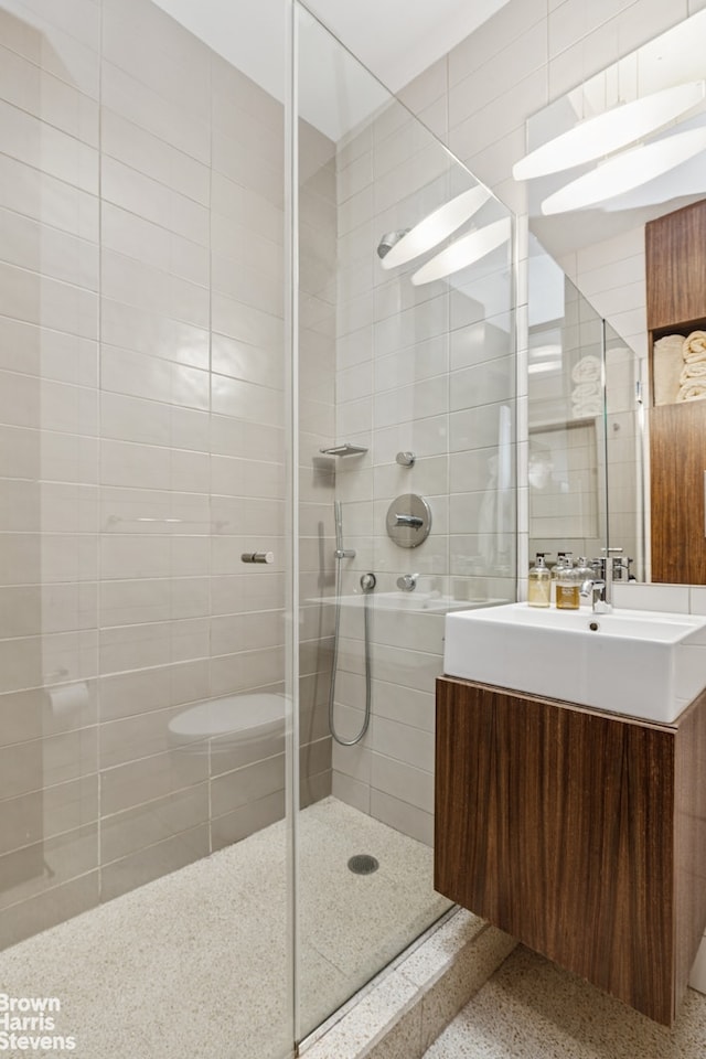 bathroom with speckle patterned floor, a tile shower, and vanity
