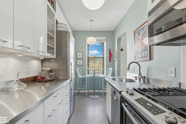 kitchen with stainless steel counters, appliances with stainless steel finishes, arched walkways, backsplash, and white cabinetry