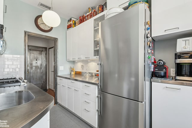 kitchen with stainless steel countertops, freestanding refrigerator, tasteful backsplash, and white cabinets