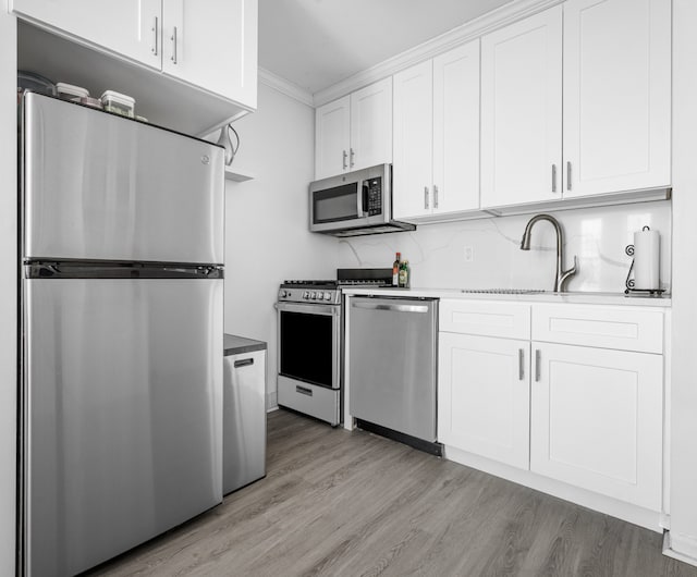 kitchen featuring appliances with stainless steel finishes, a sink, white cabinets, light wood finished floors, and ornamental molding