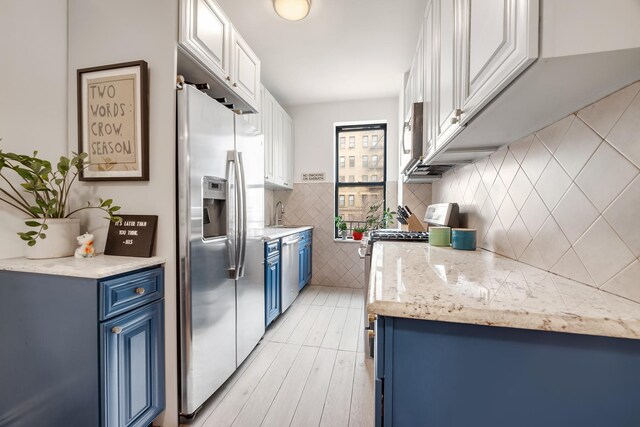kitchen featuring white cabinetry, blue cabinets, stainless steel appliances, and tasteful backsplash