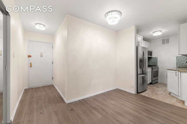 kitchen featuring stainless steel appliances, light wood-type flooring, white cabinets, and decorative backsplash