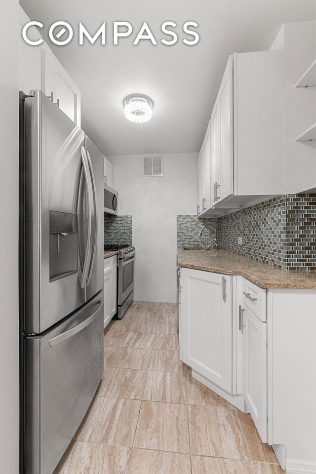 kitchen featuring stainless steel appliances, tasteful backsplash, white cabinets, and light stone countertops