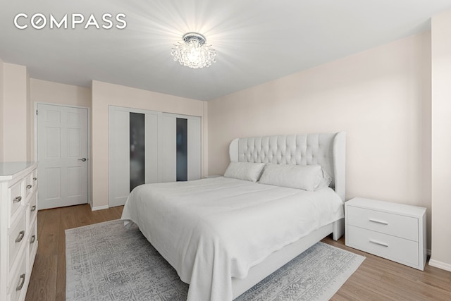 bedroom featuring light wood-type flooring, a closet, a chandelier, and baseboards