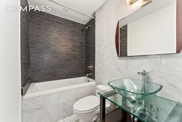 bathroom featuring a sink, toilet, tiled shower / bath combo, and tile walls