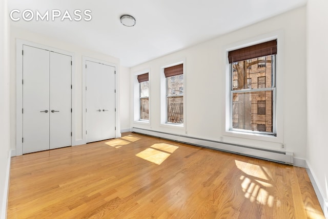 unfurnished bedroom featuring baseboard heating, multiple closets, baseboards, and wood finished floors
