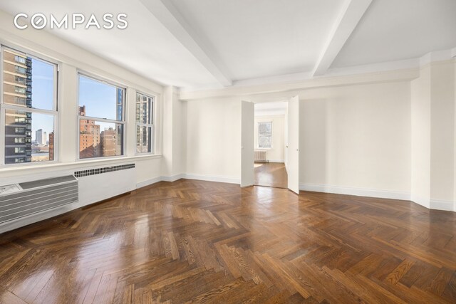 empty room with radiator heating unit, radiator, beam ceiling, and baseboards