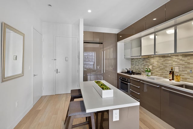 kitchen with appliances with stainless steel finishes, a kitchen bar, light countertops, and light wood finished floors