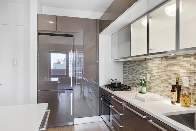 kitchen with stainless steel appliances, light wood finished floors, decorative backsplash, light countertops, and modern cabinets