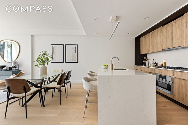kitchen with modern cabinets, a sink, light brown cabinetry, and appliances with stainless steel finishes
