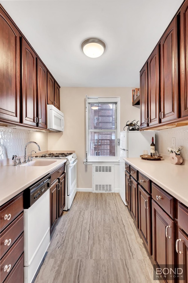 kitchen with radiator, white appliances, light wood-type flooring, a sink, and backsplash