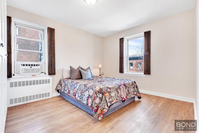 bedroom with wood-type flooring, multiple windows, and radiator heating unit